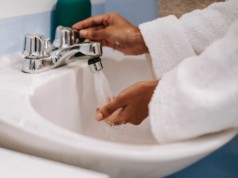 crop ethnic woman in robe washing hands in bathroom