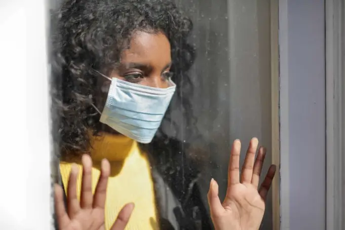 serious young ethnic lady in medical mask standing near window and looking away on street