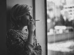 melancholic woman smoking cigarette near window during rain