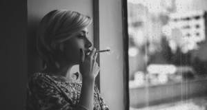 melancholic woman smoking cigarette near window during rain