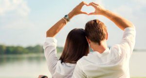 Couple making heart shape with hands outdoors.